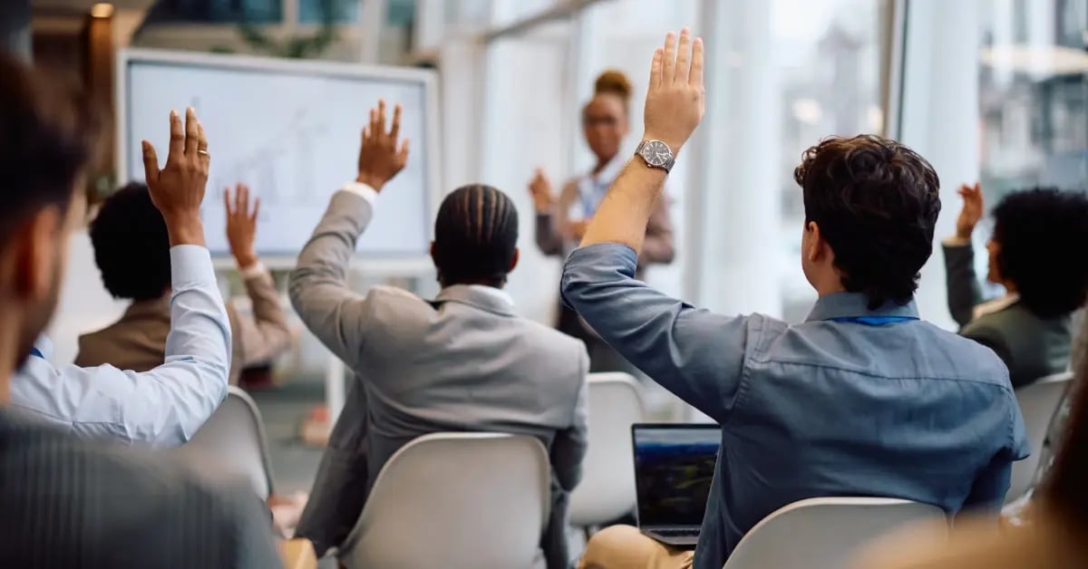 Back shot of seated attendees raising their hands a business travel conference