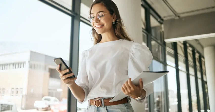 Businesswoman in a white blouse in a hallway on her mobile device and holding a stack of files