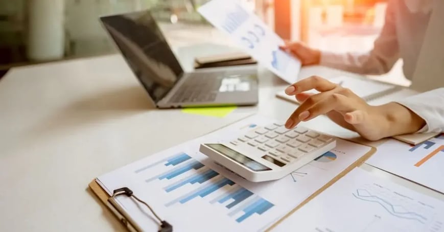 Cropped image of a woman using a calculator to manage meeting costs while holding a budget speadsheet in her other hand