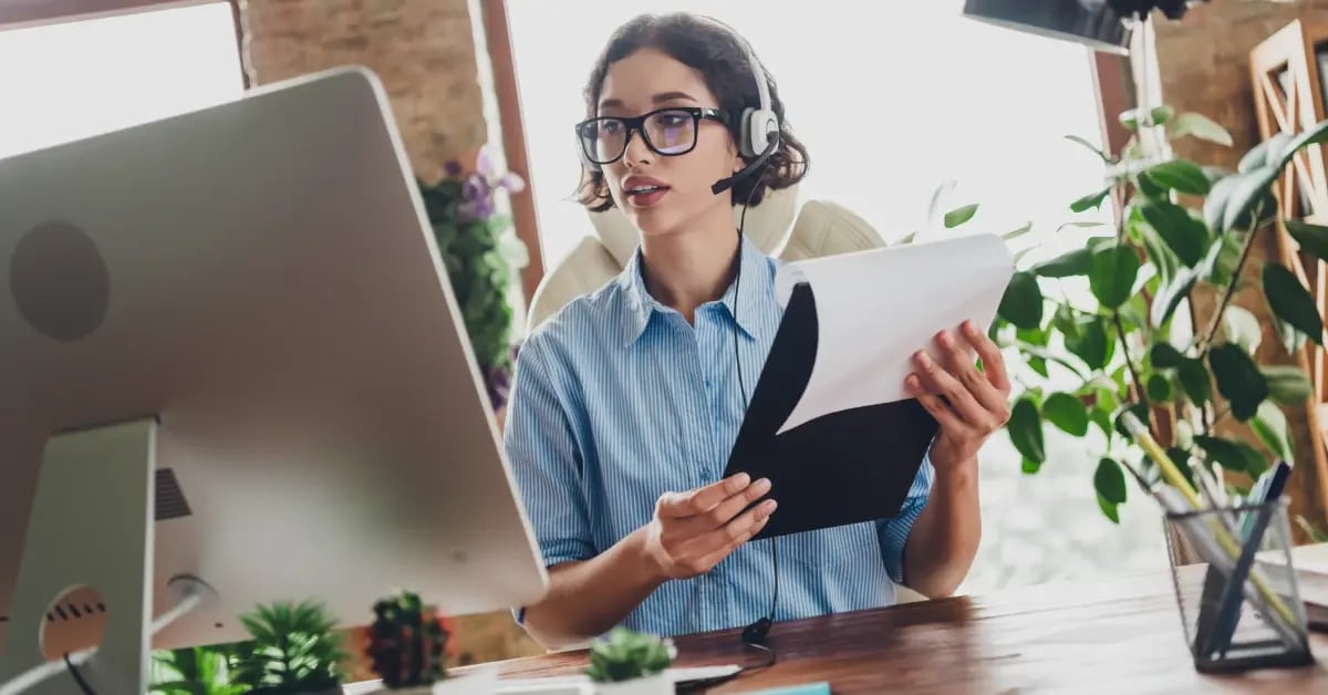 Executive Assistant working at her desk, holding a notepad, and listening to a podcast