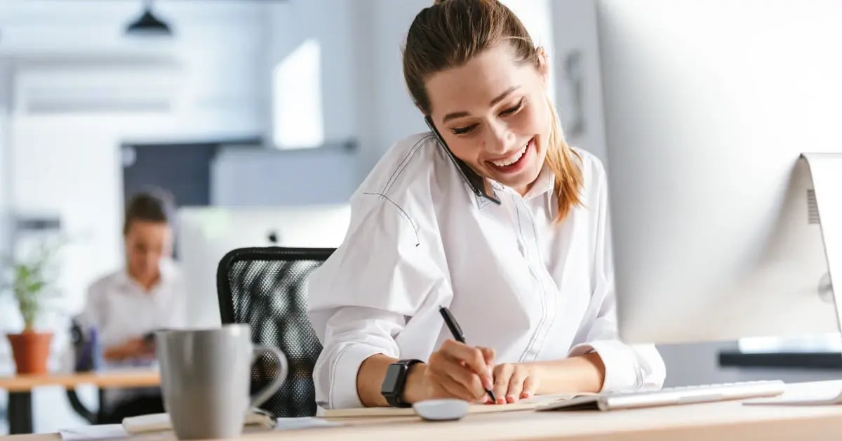 Female corporate travel planner in an office on the phone and writing in a notebook