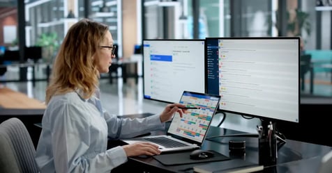Travel Manager in the office with three screens in front of her as she works to organize visibility into small meetings