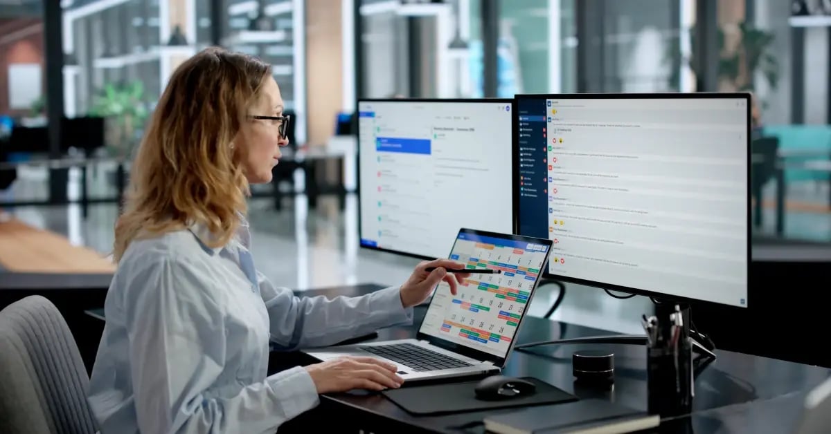 Travel Manager in the office with three screens in front of her as she works to organize visibility into small meetings