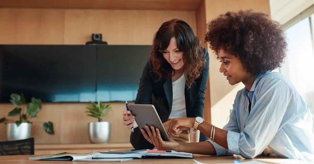 Two Executive Assistants looking at a tablet as they coordinate on an in-person meeting