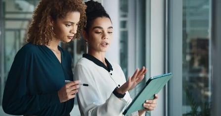 Two assistants discussing the travel budget seen on a notepad