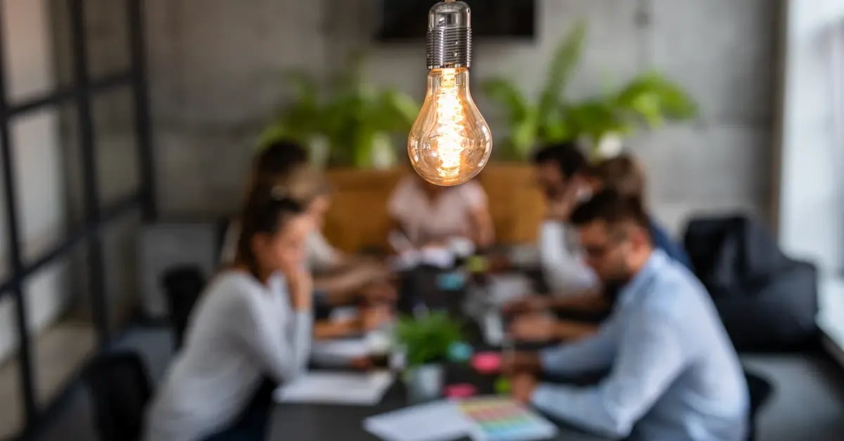 Zoomed-in lightbulb hanging while in the background is a team creating a meeting plan in an office